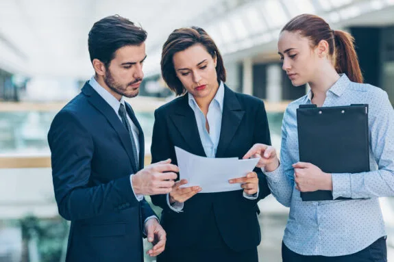 Three professionals in business attire discussing documents, emphasizing collaboration in legal matters related to trade secrets and intellectual property.